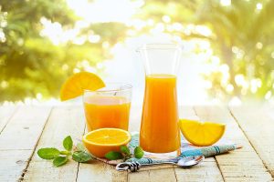 Glass and pitcher of orange juice on wooden, on green nature bac